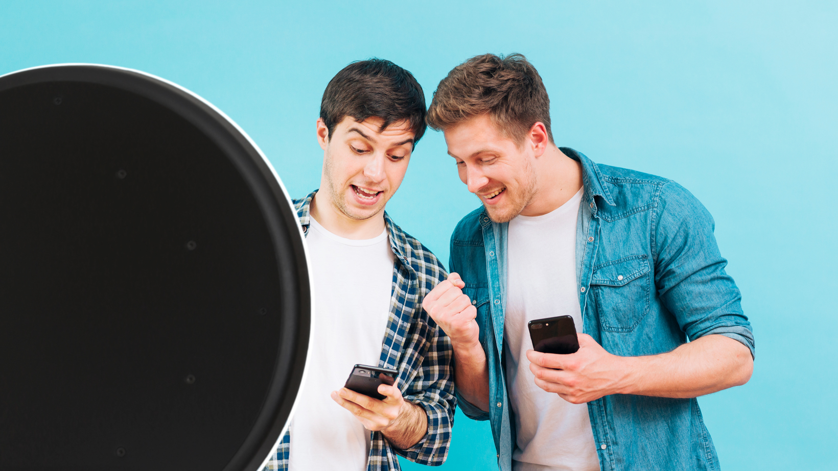 two men standing in front of a blue wall excited about what they are seeing on their phones standing in front of a black photo booth